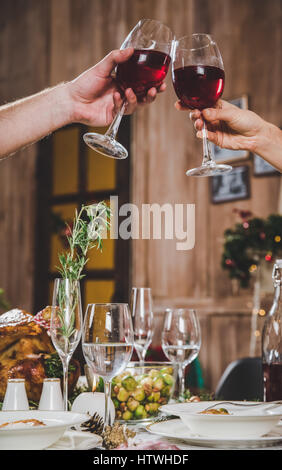 Partial view of couple toasting glasses of red wine at Christmas dinner Stock Photo