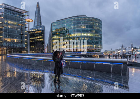 Woman taking a selfie outside in the rain under umbrella in London with view of The Shard in the City. Stock Photo