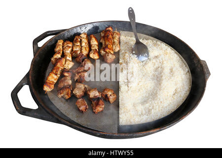 Fast street food - boiled rice and pork shish kebabs in big black iron frying pan. Isolated on white Stock Photo
