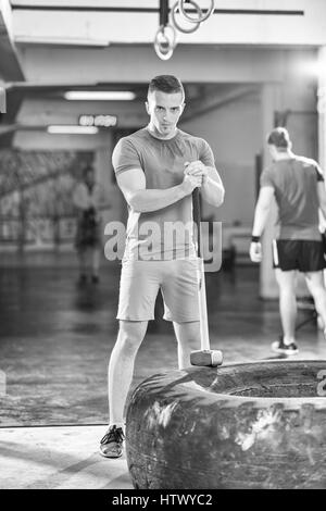 Sledgehammer Tire Hits young muscular man workout at gym with hammer and tractor tire Stock Photo