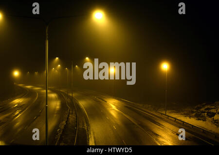 Foggy empty highway with street lights at night. Stock Photo