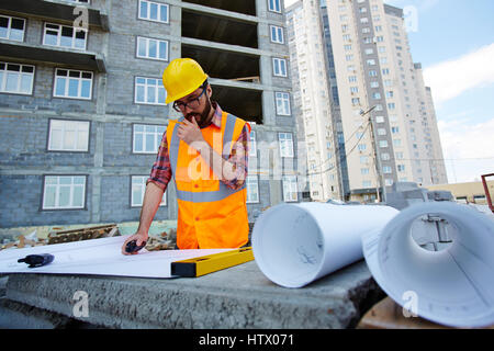 Pensive worker in hardhat and uniform looking at sketch of new building Stock Photo