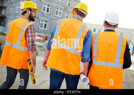 Rear view of three engineers moving towards construction-site and talking Stock Photo