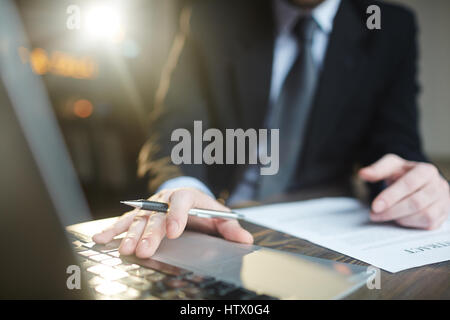 Portrait of modern successful businessman wearing black formal suit working in office with documentation, closeup shot of male hands using laptop Stock Photo