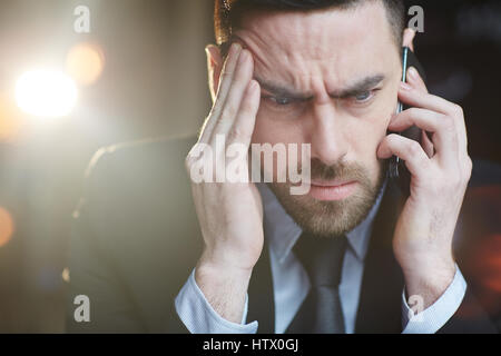 Portrait of modern bearded businessman talking by mobile phone with problem client against black lens flare background Stock Photo