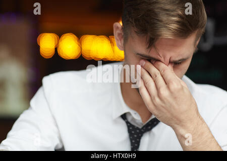 Portrait of tired young businessman wearing shirt and tie rubbing eyes and pinching nose bridge fighting headache while working late at night Stock Photo