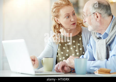 Portrait of beautiful mature woman explaining how to use computer to her grey haired husband at home Stock Photo