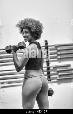 young beautiful African American woman doing bicep curls in a gym Stock Photo