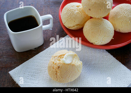 Closeup on mouth-watering Brazilian cheese bread (Pao de queijo) topped with butter on white tablecloth, other breads on red plate, on grunge wooden t Stock Photo