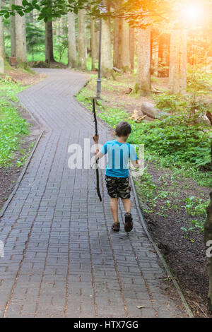 Boy with long wooden stick in forest park in sunlight Stock Photo