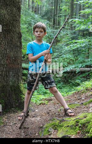 Boy with long wooden stick in forest park Stock Photo