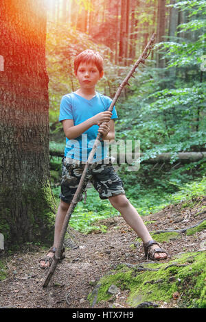 Boy with long wooden stick in forest park in sunlight Stock Photo