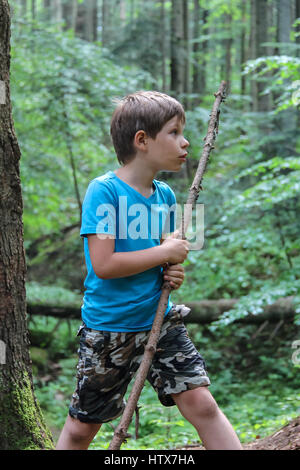 Boy with long wooden stick in forest park Stock Photo