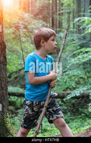 Boy with long wooden stick in forest park in sunlight Stock Photo