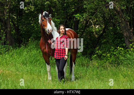 Happy country girl taking care of her horse on forest farm Stock Photo