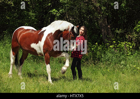 Happy country girl taking care of her horse on forest farm Stock Photo