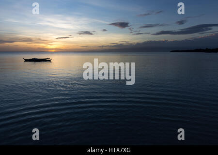 A lone traditional Filipino fisherman's pump boat floating on a perfectly still shallow sea just after sunset. Stock Photo