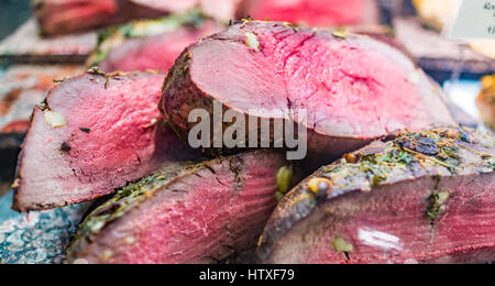 Raw pink roast beef pieces on display in market with garlic and herbs Stock Photo