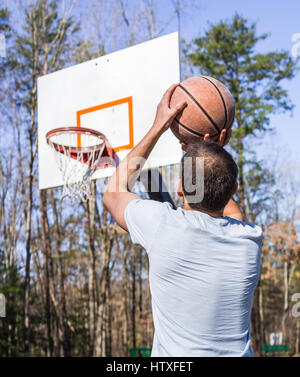 Young fit muscular man jumping up throwing basketball into hoop Stock Photo