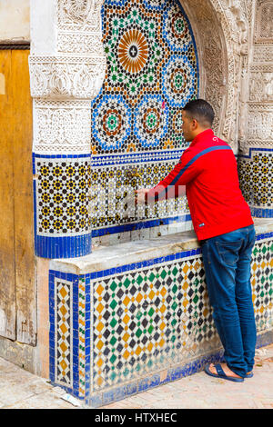 Fes, Morocco.  Place Nejjarine.  Young Man Washing Hands at the Public Fountain. Stock Photo