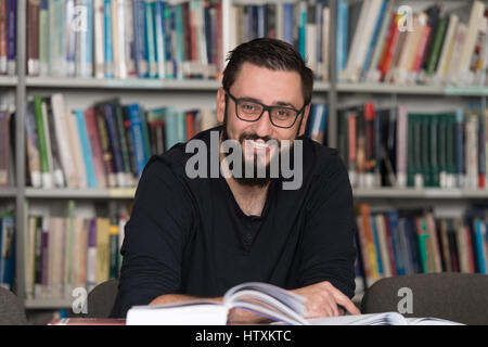 In The Library - Handsome Male Student With Laptop And Books Working In A High School - University Library - Shallow Depth Of Field Stock Photo