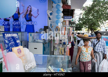 Pedestrians pass a shop selling mobile phones in Anawrahta Road, Yangon, Myanmar Stock Photo