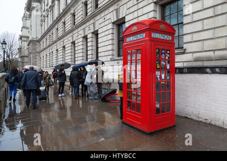 Tourists taking pictures in front of an old London telephone box on a wet and rainy day, Great George Street, SW1 Stock Photo