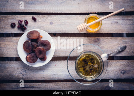 Green tea in the glass cup, dried apricots on the plate and jar of honey. Healthy breakfast. Stock Photo