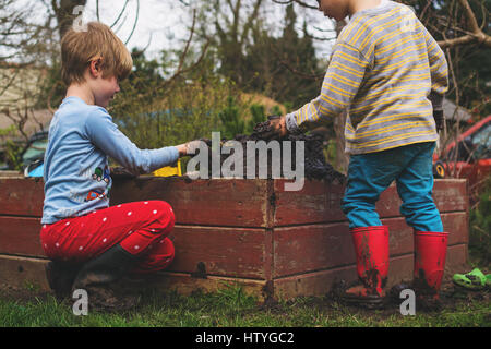 Two boys playing with mud in garden Stock Photo