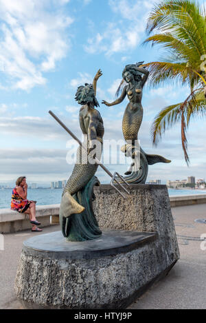 Sculpture of Triton and Mermaid by Carlos Espino (Neptune and the Nereid) on the Puerto Vallarta Malecon w/ woman in background wearing colorful dress Stock Photo