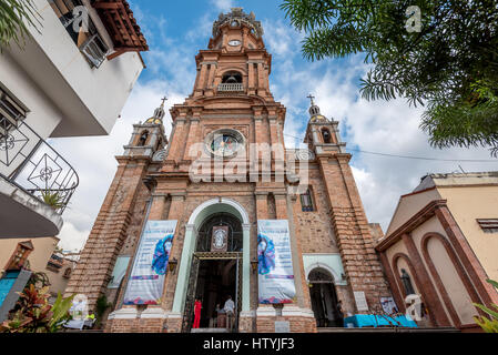 Looking up at the Puerto Vallarta church Our Lady of Guadalupe from close up with wide angle lens and full corners, lady in red standing in  doorway. Stock Photo