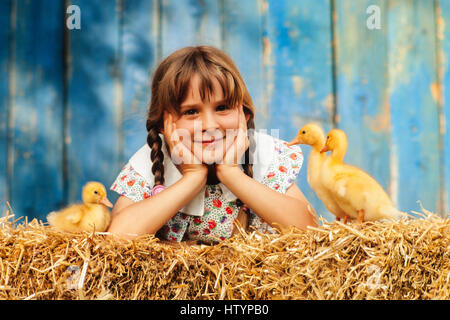 Nine year old girl lying with three ducklings in the straw, Austria Stock Photo
