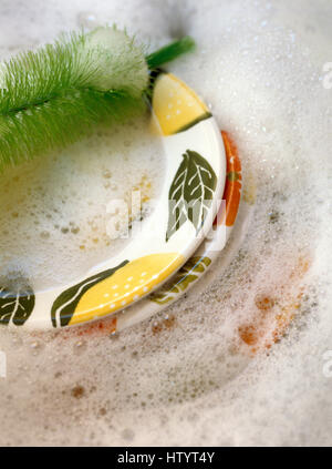 Close-up of hand painted plates in a washing up bowl with soap suds and a green washing up brush Stock Photo
