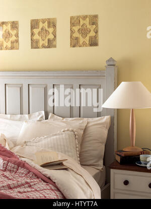Decorative collage pictures on wall above a grey painted bed piled with cushions Stock Photo