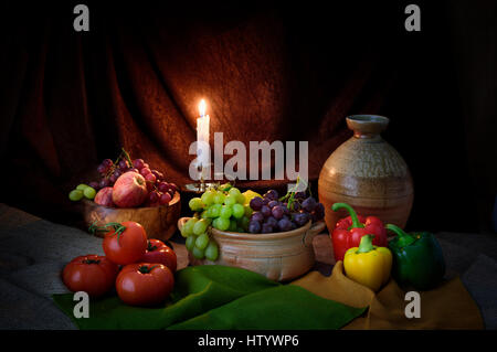 Candle lit still life photograph of fruit and vegetables in style of old master  of apples tomatoes grapes candle light and rustic pottery Stock Photo