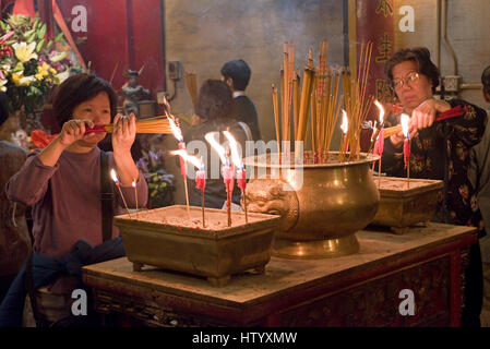 Local people at the Man Mo Temple in Hong Kong lighting incense sticks prior to prayer with candels burning. Stock Photo