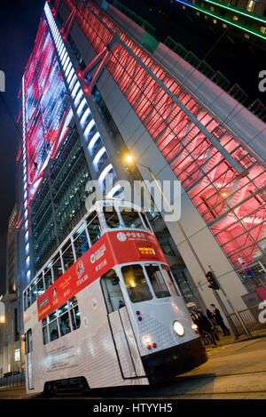 An abstract view of a Hong Kong tram travelling along a street in the business district with skyscrapers in the background at night. Stock Photo