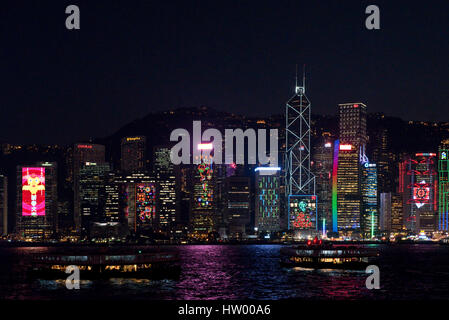 A cityscape view of the buildings along Hong Kong Island with 2 Star Ferries in the foreground at night. Stock Photo