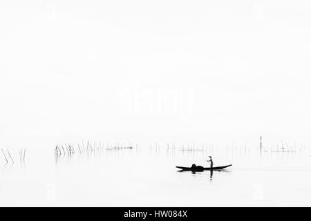 Traditional fishing boat on Lake at Sunrise, Fog Rising from Water - Vietnam Stock Photo