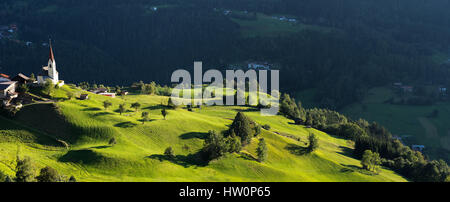 Chapel and sheep on the meadow. Bell tower, trees, shrubs and hilly green grassland. Heiliger Antoniuse church and houses in the evening light. Piburg Stock Photo