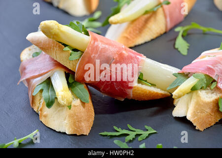 Delicious morsels with white asparagus on rocket leaves wrapped with Italian prosciutto Stock Photo