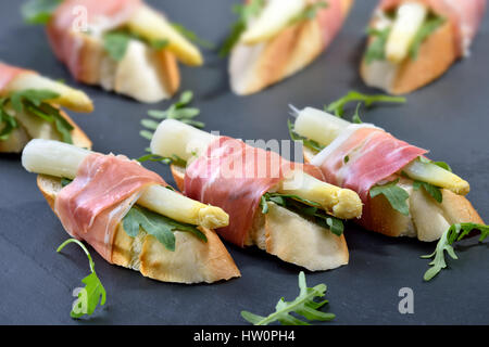 Delicious morsels with white asparagus on rocket leaves wrapped with Italian prosciutto Stock Photo