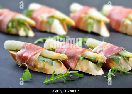 Delicious morsels with white asparagus on rocket leaves wrapped with Italian prosciutto Stock Photo