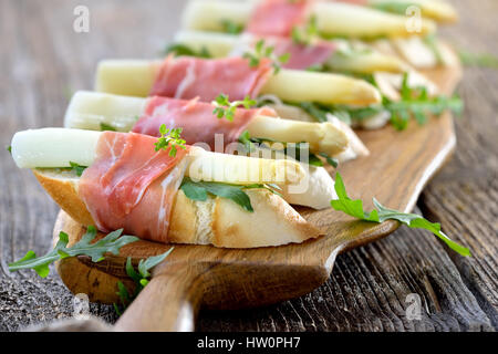 Delicious morsels with white asparagus on rocket leaves wrapped with Italian prosciutto Stock Photo