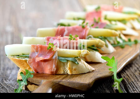 Delicious morsels with white asparagus on rocket leaves wrapped with Italian prosciutto Stock Photo