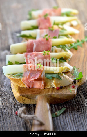 Delicious morsels with white asparagus on rocket leaves wrapped with Italian prosciutto Stock Photo