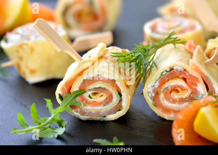 Rolls of thin pancakes with smoked salmon, horseradish cream cheese and rocket leaves Stock Photo