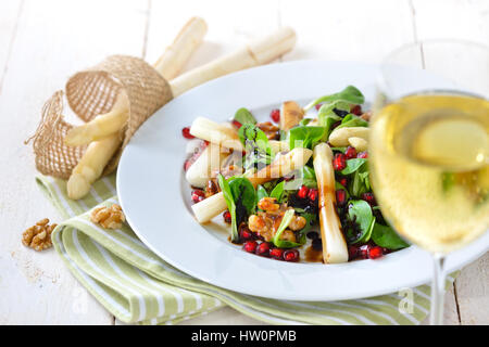 White asparagus on lamb's lettuce with candied walnuts, pomegranate seeds and balsamic vinegar, served with a glass of fruity white wine Stock Photo