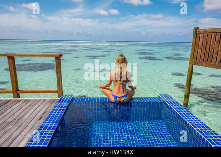 Maldives, Rangali Island. Conrad Hilton Resort. Woman in pool with view of the ocean and the back deck of the water villa. Stock Photo