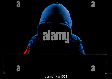 Faceless hacker with laptop in black isolated background. Stock Photo
